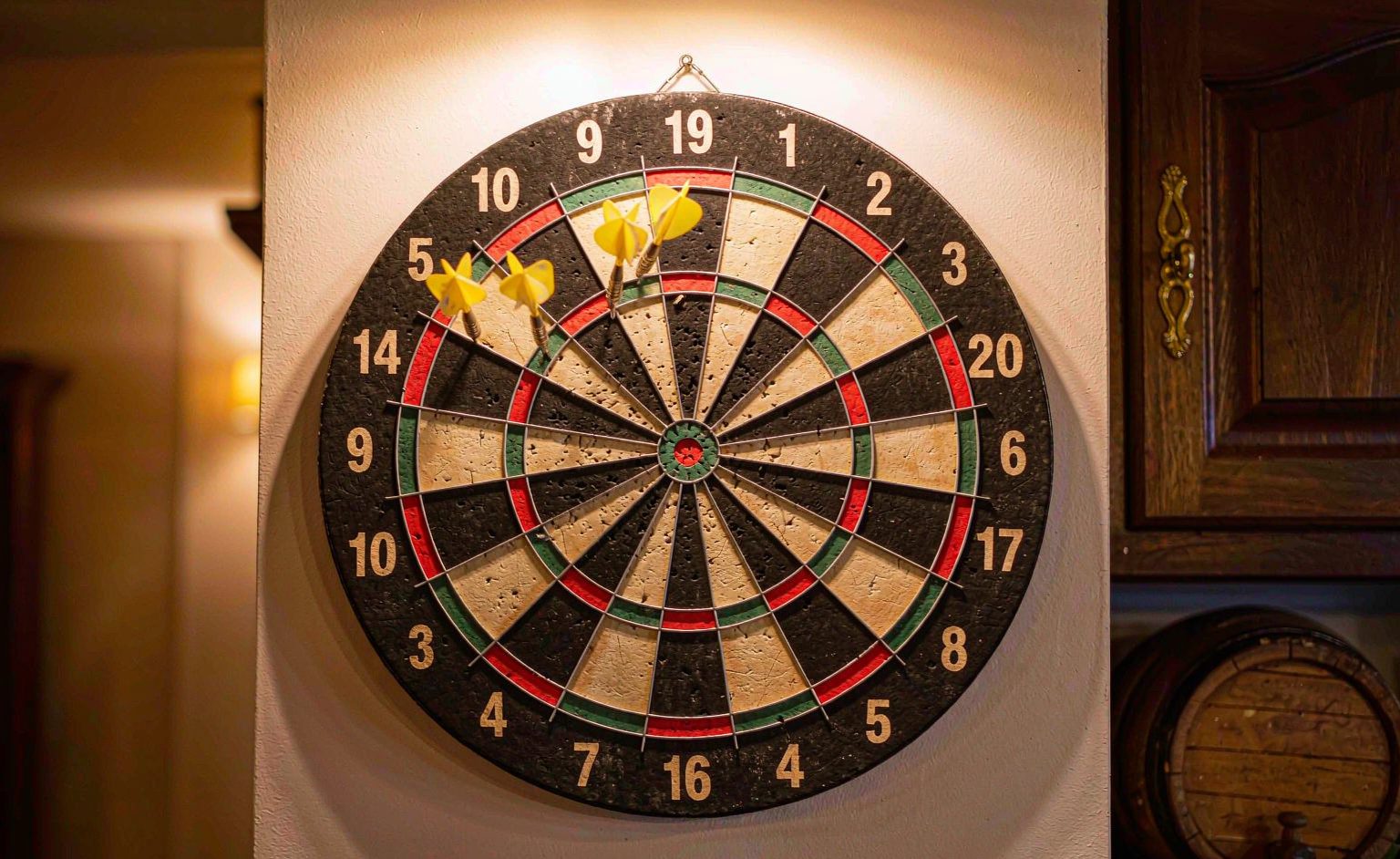 Bristle dart board mounted on a wall with steel tip darts in the bullseye area