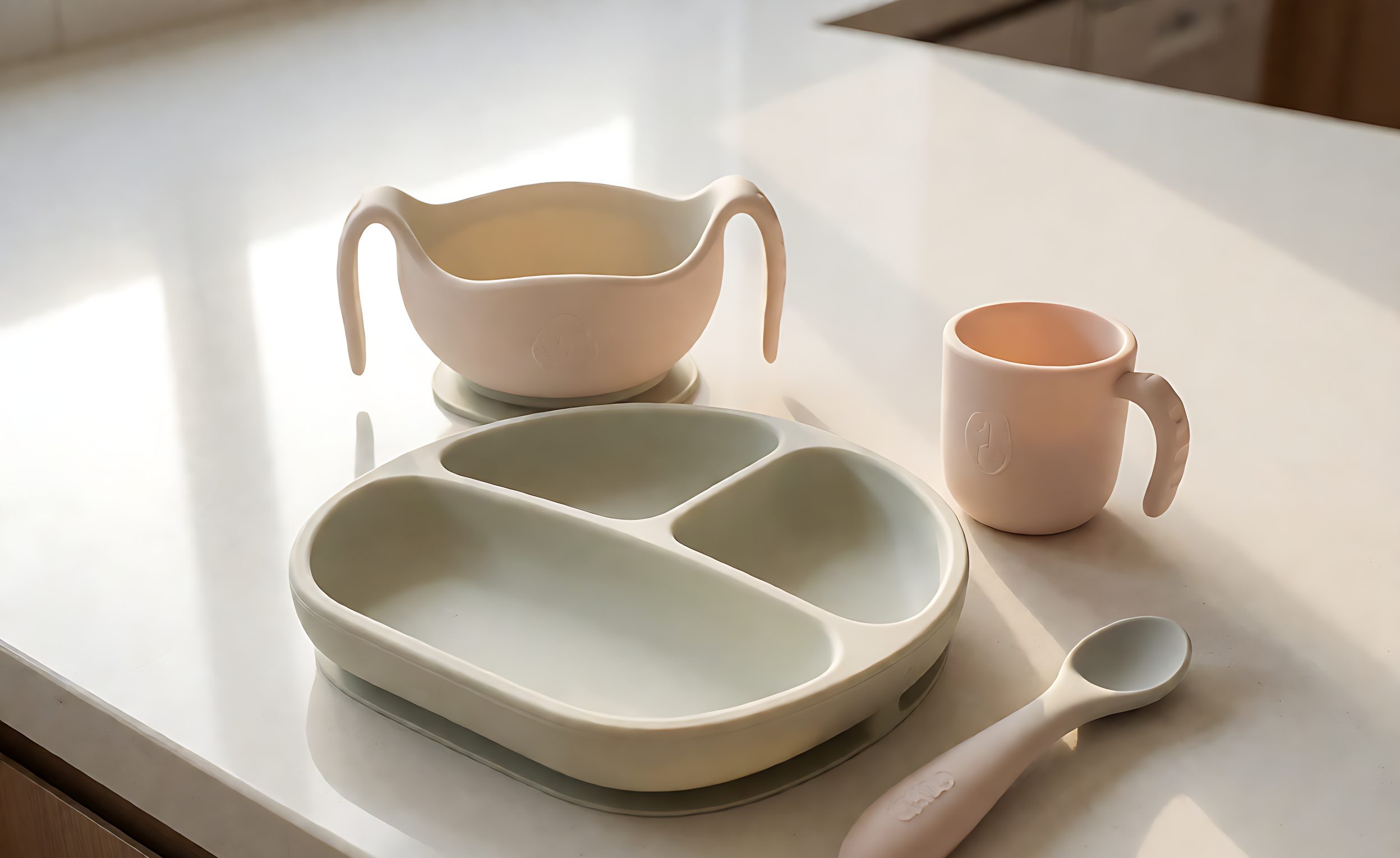 Pastel silicone baby feeding set with suction bowl, plate, cup and spoon on a counter